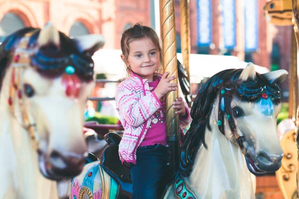 Kleine schattige glimlachende meisje rijden een paard op de rotonde carous — Stockfoto