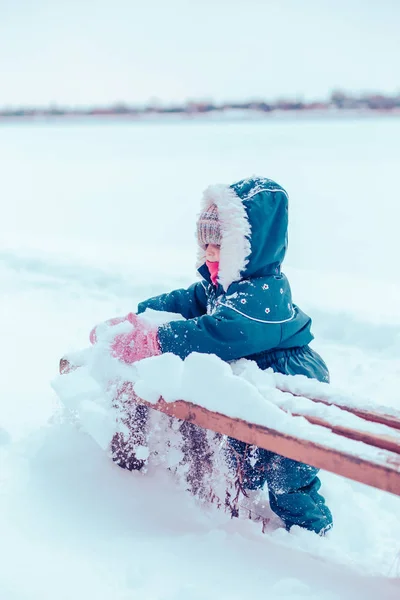 Klein meisje genieten winter het verwijderen van sneeuw uit een bankje — Stockfoto