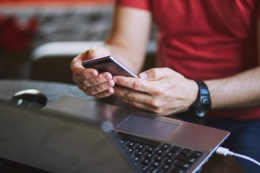 Dizüstü bilgisayarda çalışan akıllı telefonu kullanan adam