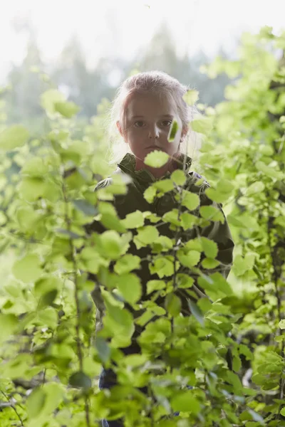 Niña parada en el bosque detrás de las hojas —  Fotos de Stock