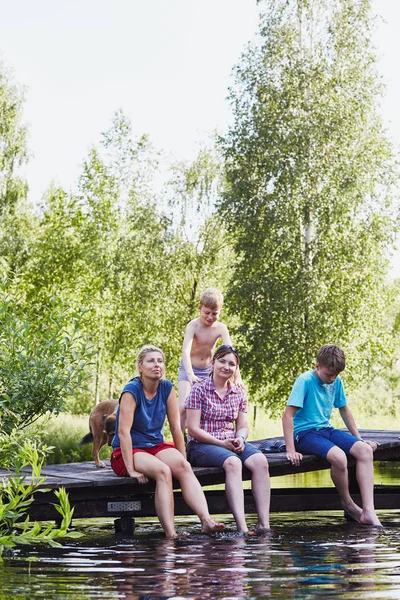Family sitting on a bridge over a lake during summer vacations — Stock Photo, Image