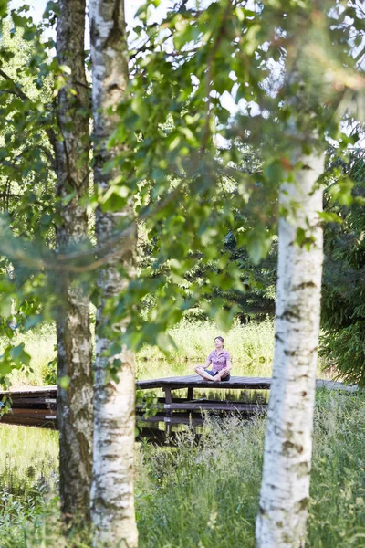 Kvinna sitter på en bro över en sjö under sommarsemester — Stockfoto