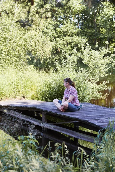 Femme assise sur un pont au-dessus d'un lac pendant les vacances d'été — Photo