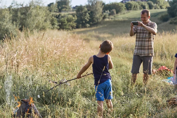 Hombre tomando una foto a su hijo asando malvavisco sobre una fogata —  Fotos de Stock