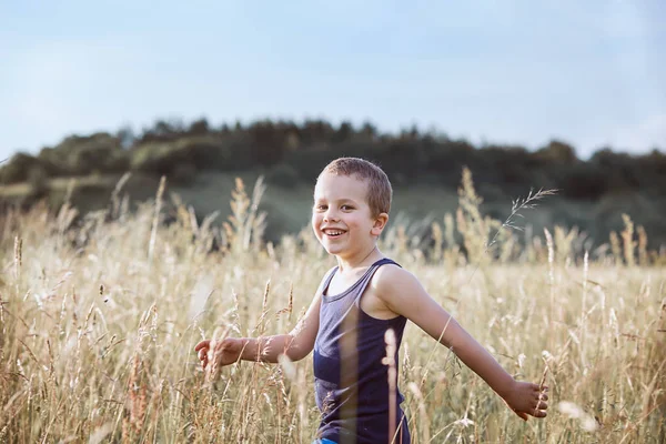 Petit garçon heureux marchant à travers une grande herbe dans la campagne — Photo