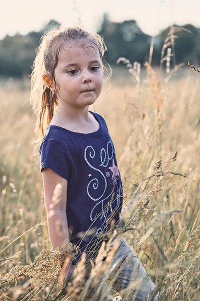 Lite glad leende flicka som leker i ett högt gräs — Stockfoto