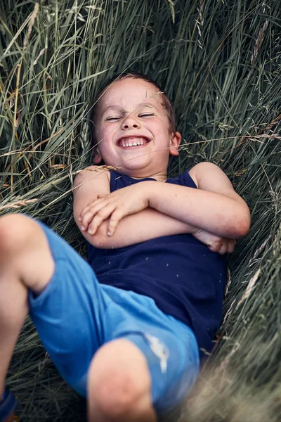 Petit garçon souriant heureux jouant dans une herbe haute — Photo