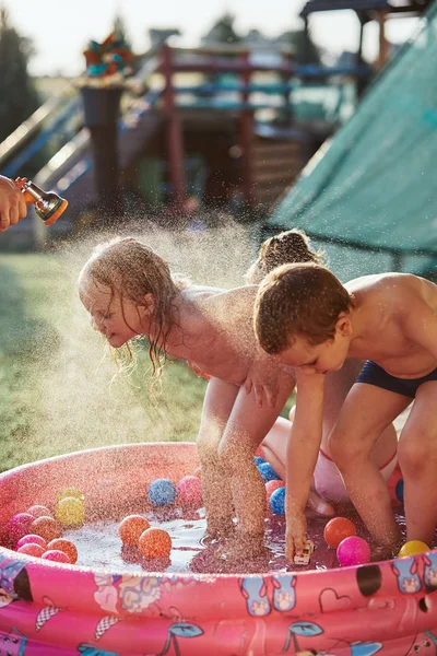 Küçük çocuklar babaları tarafından püskürtülen serin suyun tadını çıkarıyorlar. — Stok fotoğraf