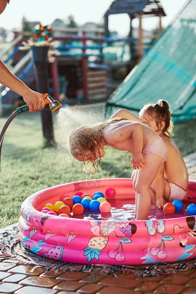 Little girls enjoying a cool water sprayed by their father — Stock Photo, Image