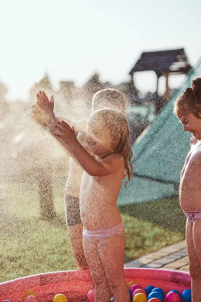 Little kids enjoying a cool water sprayed by their father — Stock Photo, Image