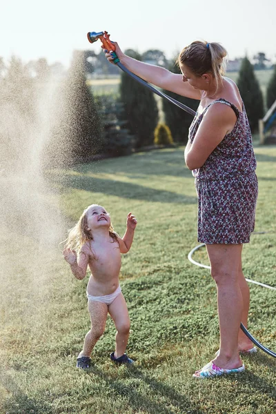 彼女の母親によってスプレー冷たい水を楽しむ小さな女の子 — ストック写真