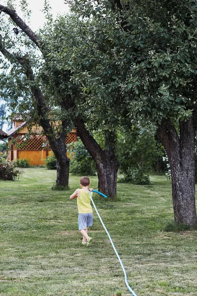 Pojke dra en trädgårdsslang för att vattna växterna — Stockfoto