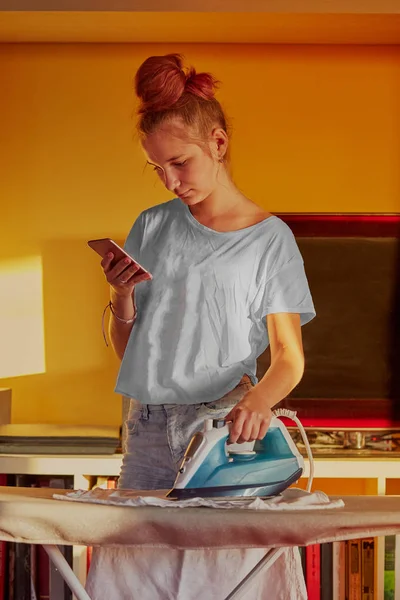 Young woman is ironing her clothes and talking on a  smartphone — Stock Photo, Image