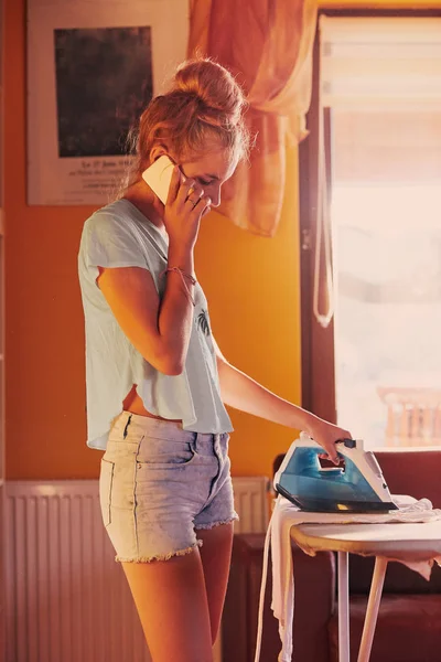 Mujer joven está planchando su ropa y hablando en un teléfono inteligente — Foto de Stock