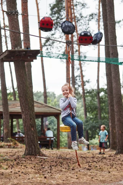 Happy girl riding on the zip line in rope park — Stock Photo, Image