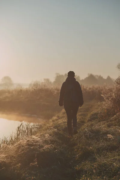 Sun rising above field and pond flooded with fog