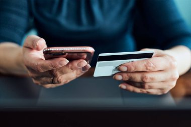 Kadın banka kartı ve dizüstü bilgisayar kullanarak online alışveriş yapıyor. Bilgisayarın klavyesinde elinde kredi kartı olan bir kadın masadan internetten mal alıyor.