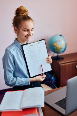 Ödev yapan genç bir kız öğrenci, derslere giriyor, çevrimiçi öğreniyor, uzaktan ders izliyor, profesörü dinliyor, karantina sırasında okuldan arkadaşlarıyla konuşuyor. Dizüstü bilgisayar, kulaklık, kitap, el kitabı kullanan genç bir kız oturuyor.