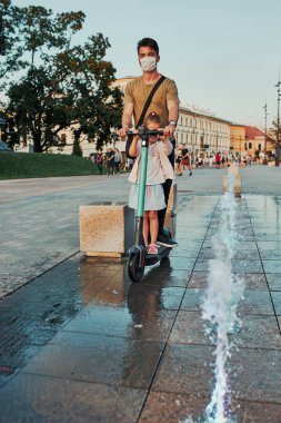 Genç bir adam ve kız kardeşi şehir merkezinde elektrikli scooter kullanıyor. Virüs enfeksiyonunu önlemek ve koronavirüs zamanında hastalığın yayılmasını önlemek için yüz maskesi takan adam. Samimi insanlar, gerçek anlar, otantik durum