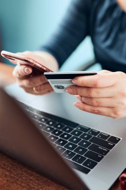 Kadın banka kartı ve dizüstü bilgisayar kullanarak online alışveriş yapıyor. Bilgisayarın klavyesinde elinde kredi kartı olan bir kadın masadan internetten mal alıyor.
