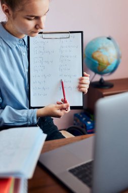 Ödev yapan genç bir kız öğrenci, derslere giriyor, çevrimiçi öğreniyor, uzaktan ders izliyor, profesörü dinliyor, karantina sırasında okuldan arkadaşlarıyla konuşuyor. Dizüstü bilgisayar, kulaklık, kitap, el kitabı kullanan genç bir kız oturuyor.