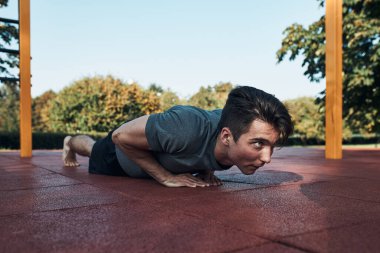 Modern bir jimnastik parkında antrenman yaparken kırmızı lastik zeminde şınav çeken genç bir adam. Spor giyinmiş bir adam başka tarafa bakıyor.