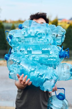Genç adam kullanılmış plastik su şişelerini çöp kutusuna atıyor. Geri dönüşüm için plastik atık topluyorum. Plastik kirliliği ve çok fazla plastik atığı kavramı. Çevre sorunu