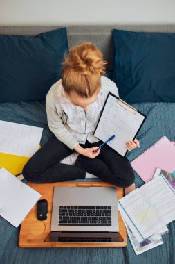 Sınıfı olan genç bir kız öğrenci, internetten öğreniyor, uzaktan ders izliyor, profesörü dinliyor, karantina sırasında okuldan arkadaşlarıyla konuşuyor. Laptop, kulaklık, kitap ve el kitabı kullanan genç bir kız.