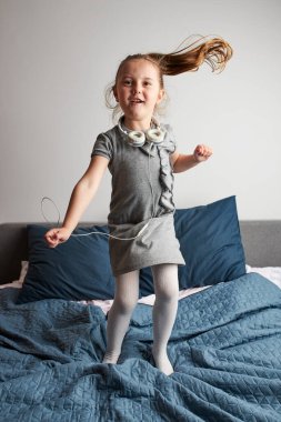 Kulaklıkla şarkı söyleyen küçük kız kendini gerçek bir şarkıcı gibi gösteriyor. Çocuk zıplayarak, dans ederek, yatakta müzik dinleyerek eğleniyor.