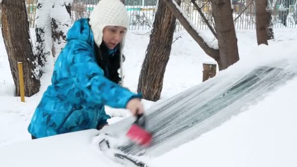 Дівчина прибирає машину зі снігу — стокове відео