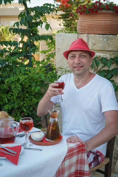 Kırmızı şapkalı bir adam restoranda bir bardak şarap tutuyor. Girit Adası.