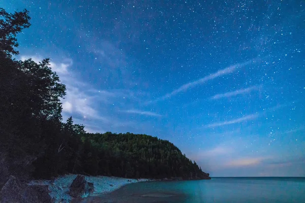 Voie lactée et ciel étoilé avec des nuages tortueux le long du bord du lac o — Photo