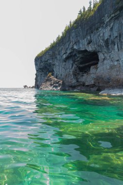 Bright clear aqua green water on Bruce Peninsula. Crystal clear water shows big limestone rocks and cliff clipart