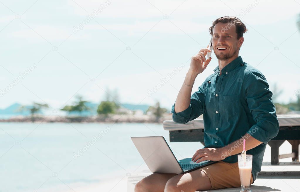 Man freelancer with laptop and mobile phone sitting at the beach