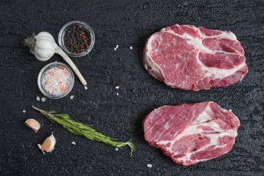 Siyah taş zemin üzerine taze çiğ kemiksiz domuz eti boyun dilimleri. Üstten görünüm.