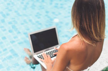 Havuz kenarında otururken ona dizüstü bilgisayar üzerinde çalışan kadın serbest meslek