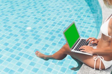 Havuz kenarında otururken ona dizüstü bilgisayar üzerinde çalışan kadın serbest meslek