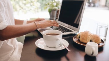 Genç kadın öğrenci kafede oturan ve kahvaltı laptop ile çalışan dizüstü bilgisayar ile