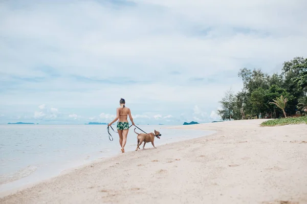 ビーチで彼女の犬を連れて歩いて陽気な若い女性 — ストック写真