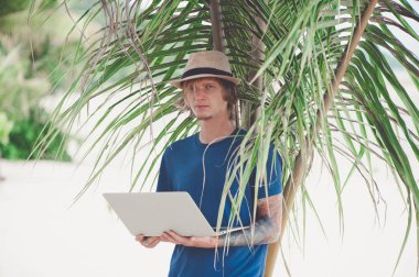 Güneş gözlüğü ve laptop ile plajda çalışan bir şapka giyen yakışıklı sarışın adam