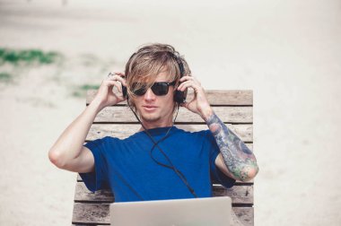 Güneş gözlüğü ve laptop ile plajda çalışan bir şapka giyen yakışıklı sarışın adam