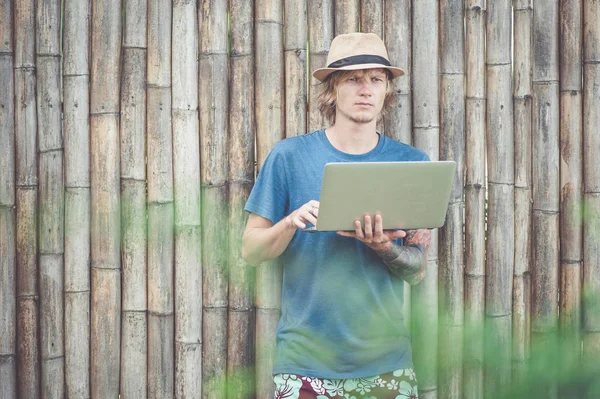 Handsome man in hat working with laptop at the bamboo wall