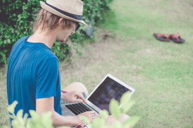 Güneş gözlüğü ve laptop ile plajda çalışan bir şapka giyen yakışıklı sarışın adam