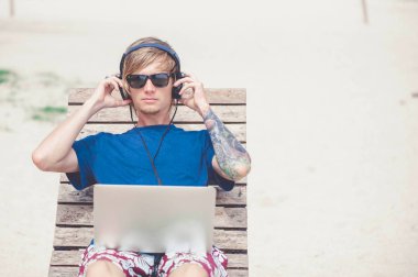 Güneş gözlüğü ve laptop ile plajda çalışan bir şapka giyen yakışıklı sarışın adam