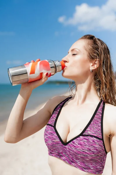 Fitness beautiful woman drinking water and sweating after exercising on summer hot day in beach.