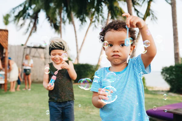 Little boys with soap bubbles in tropical garden — Stock Photo, Image