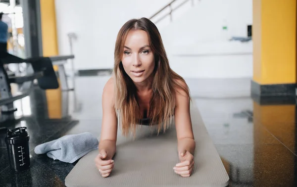 Aantrekkelijke jonge vrouw doet plank oefening in de gym — Stockfoto