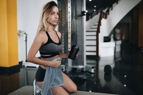 Fitness femme boire de l'eau tout en se reposant sur le sol dans la salle de gym . — Photo