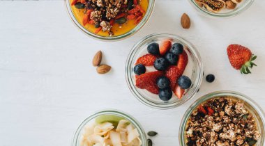 Beyaz arka planda yoğurt, granola ve farklı MEYVELERLE kase