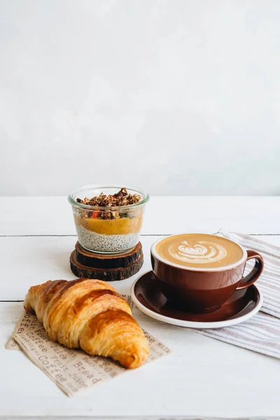 Смачний сніданок на столі. Чашка кави, манго Чіа пудинг і круасан за білим столом . — стокове фото